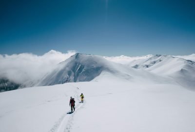 Two hikers traverse a snowy mountain under a clear blue sky, capturing the spirit of adventure.